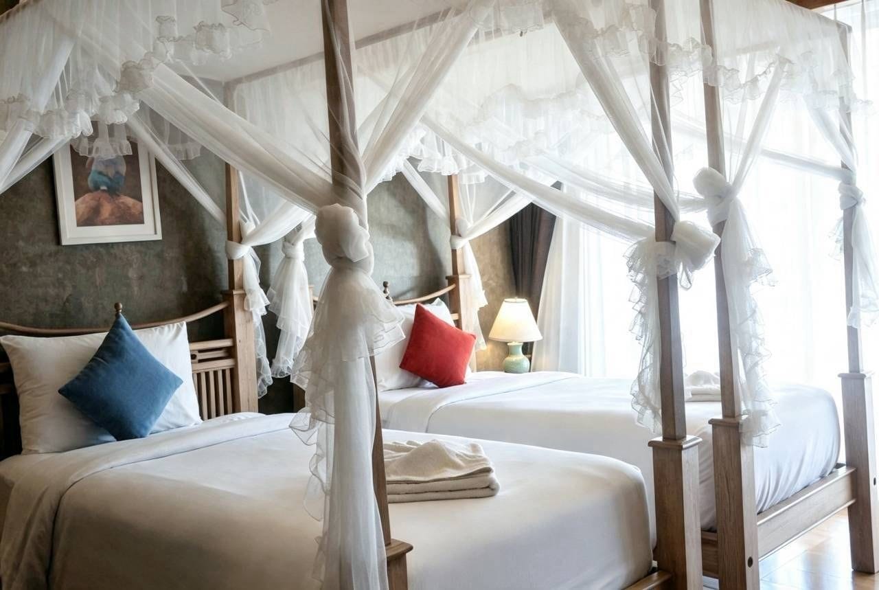A four-poster canopy bed with white linens and a red pillow, a bedside table with a lamp, and a framed picture on the wall.