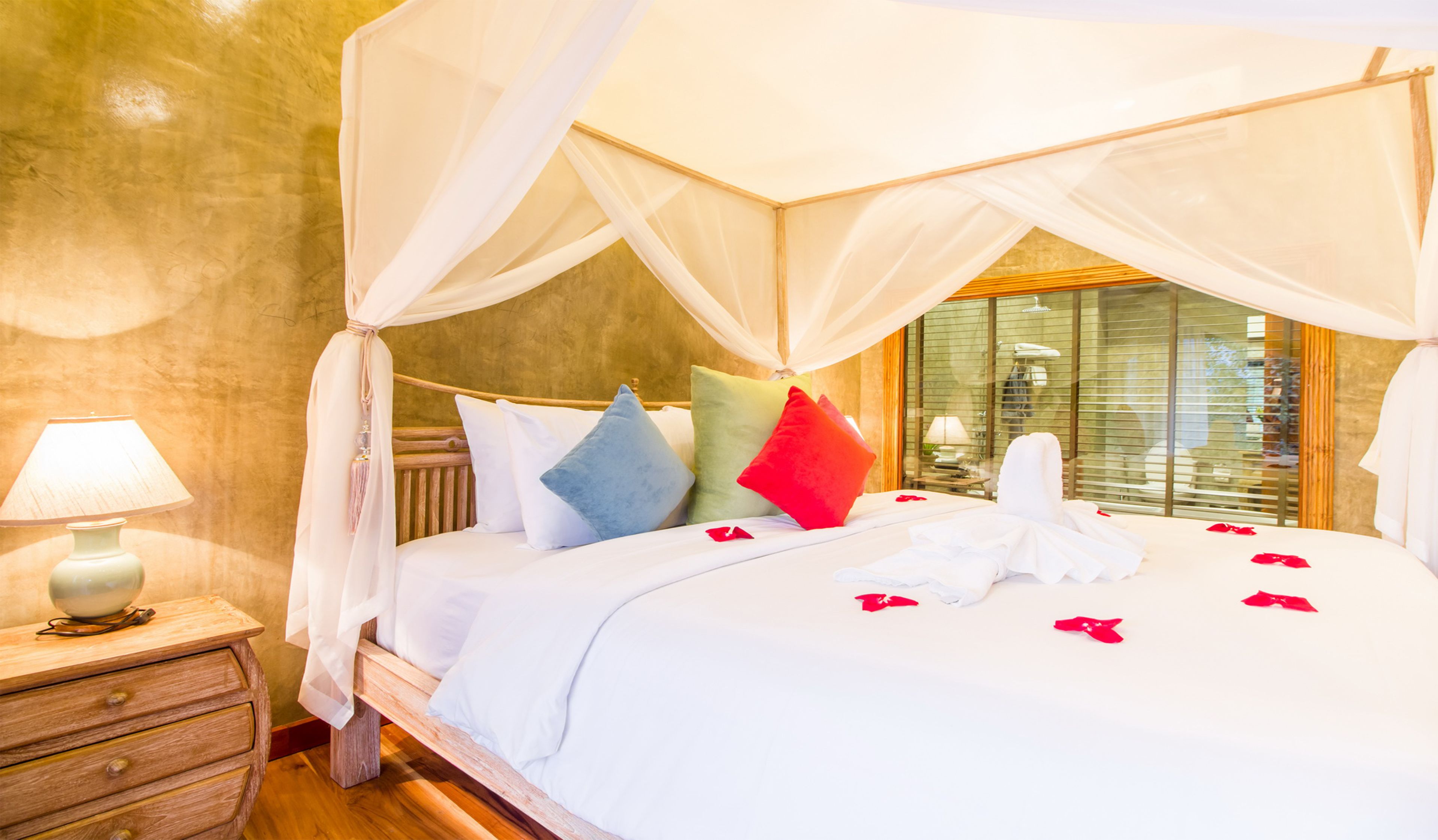 A bed with a canopy, pillows, and rose petals.