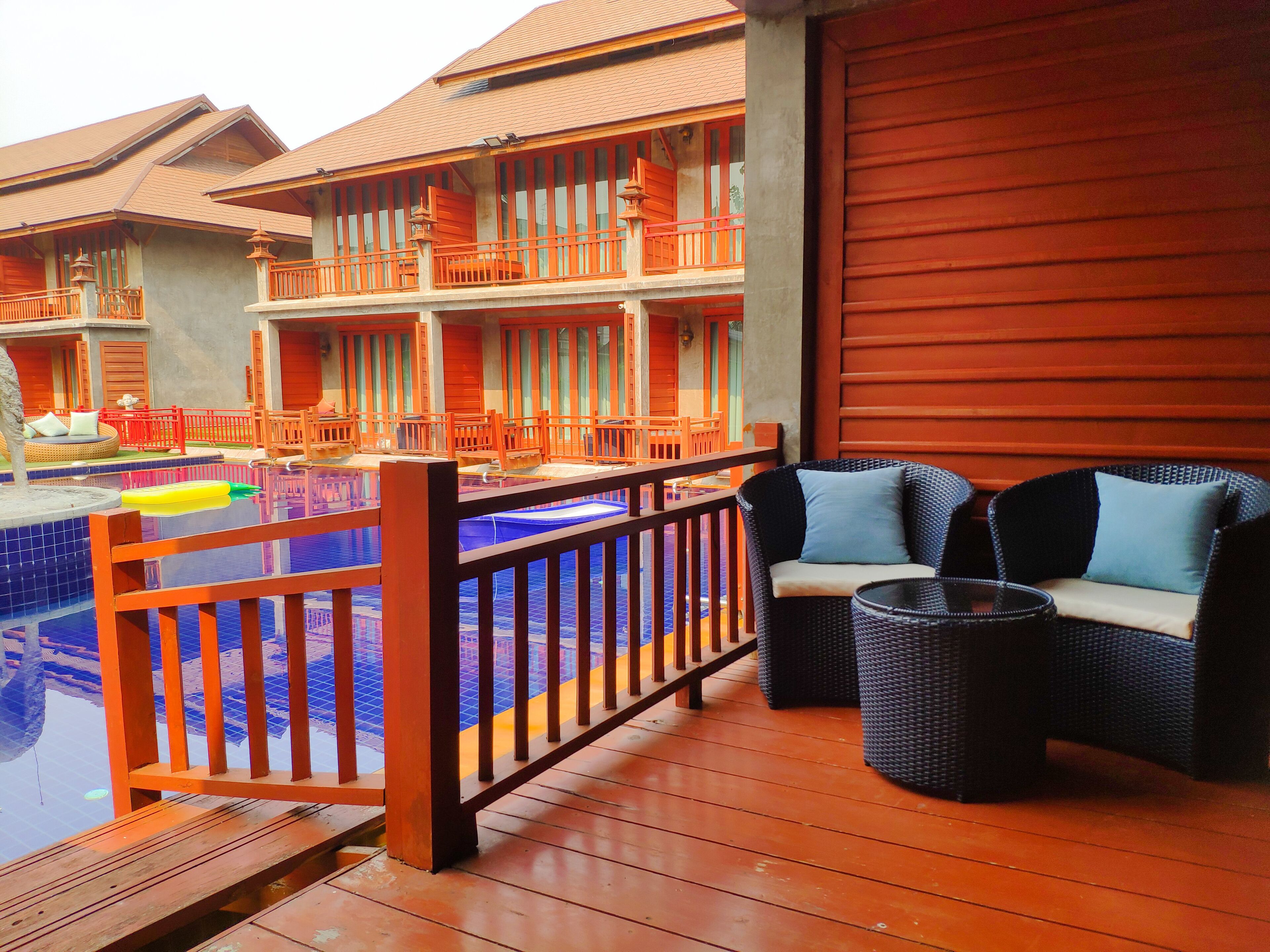 A wooden deck with a pool, outdoor furniture, and a building with multiple balconies.
