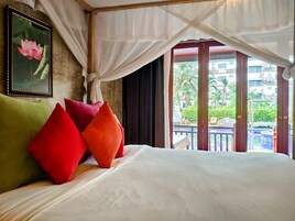 Una cama con almohadas coloridas, un cuadro con una flor de loto y vistas a un balcón con piscina.