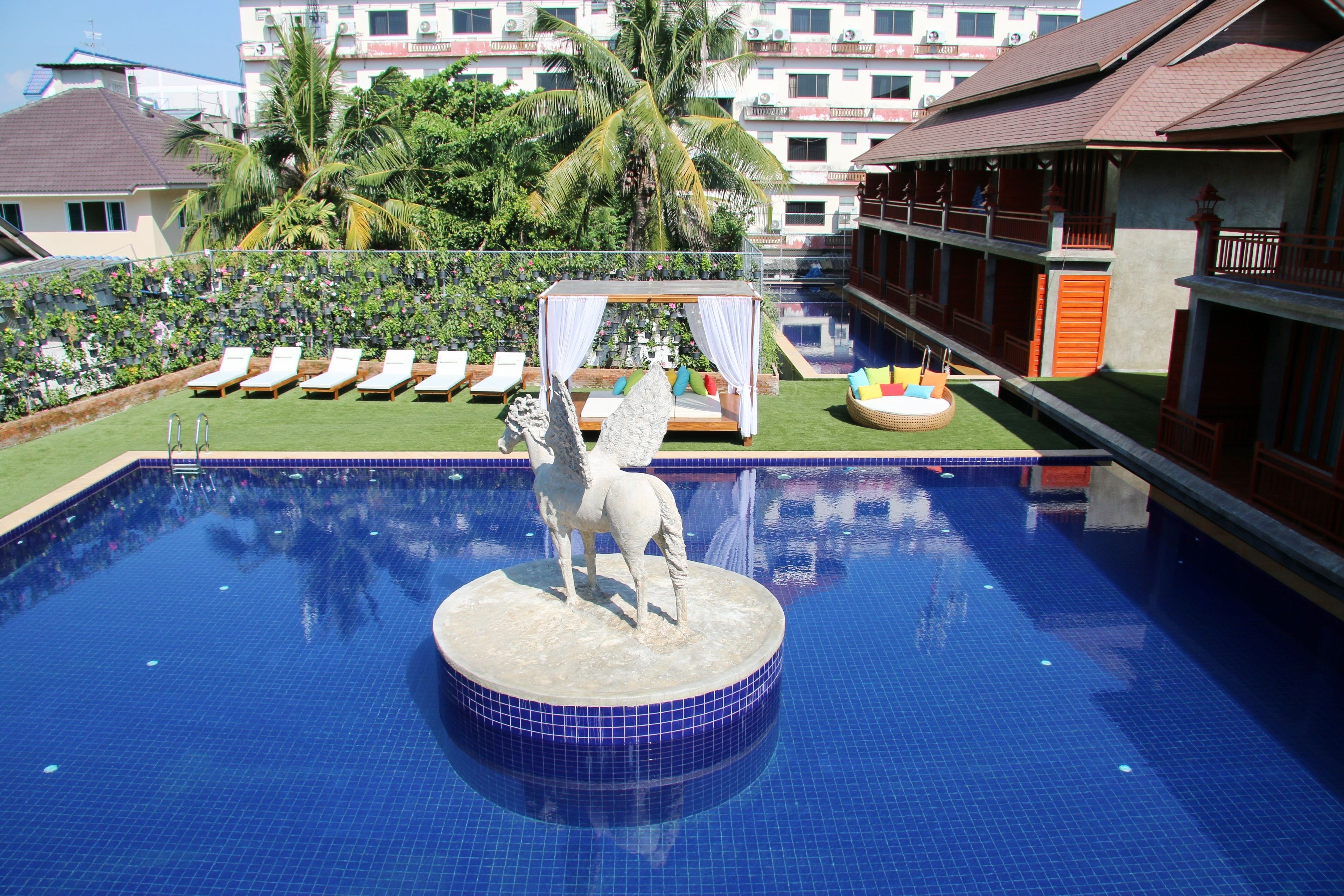 A swimming pool with a statue of a horse, lounge chairs, and a bed with a canopy.