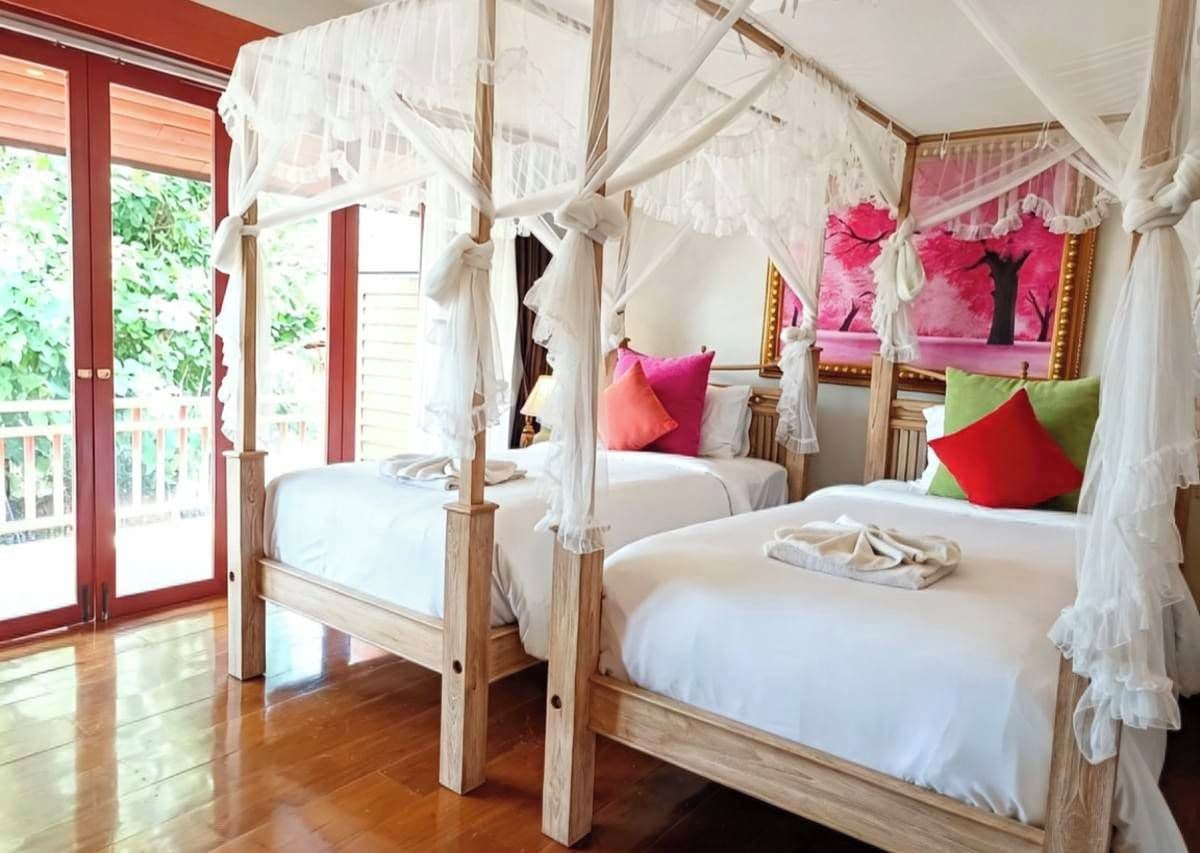 A room with two wooden beds, each with a canopy, and a large window with a view of greenery.