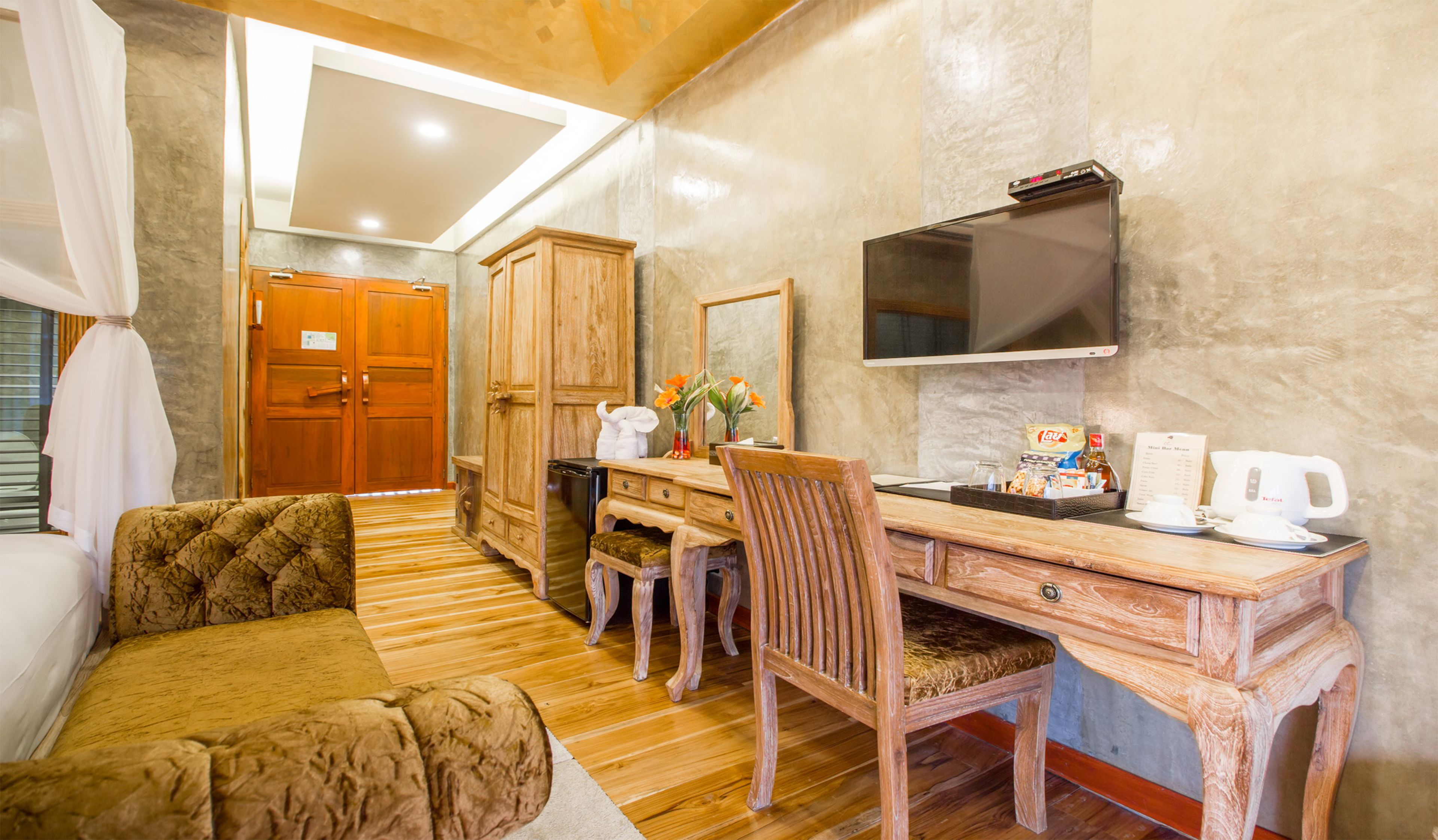 A cozy room with a wooden desk, a comfortable sofa, a television, and a minibar.