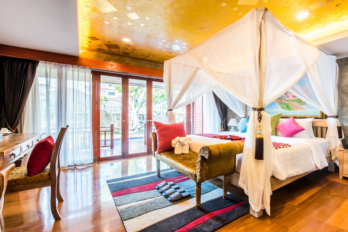 Ein geräumiges Schlafzimmer mit einem Himmelbett, einem Holfnachtkästchen und Blick ins Freie durch große Schiebetüren.