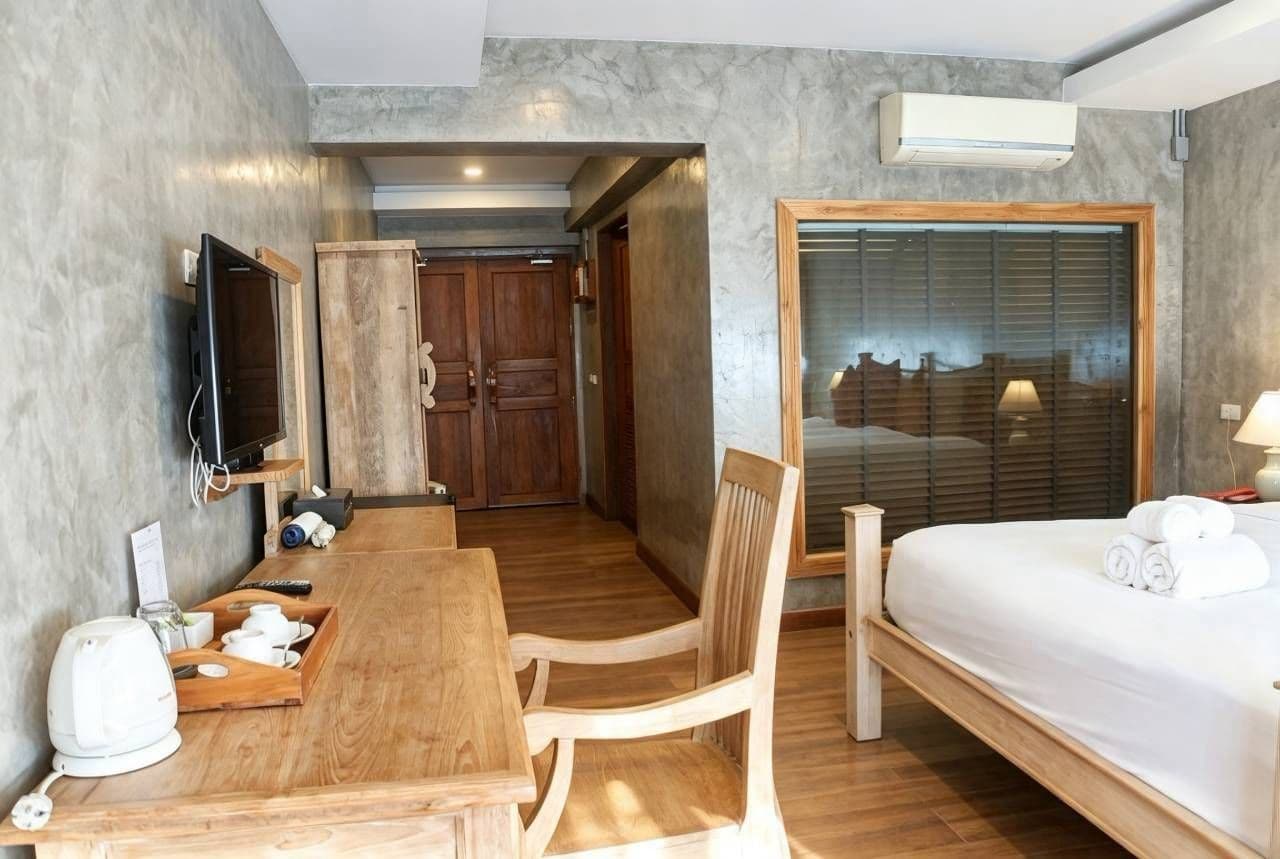 Habitación de hotel con una cama de madera, un escritorio con silla, un televisor y una ventana con persianas.