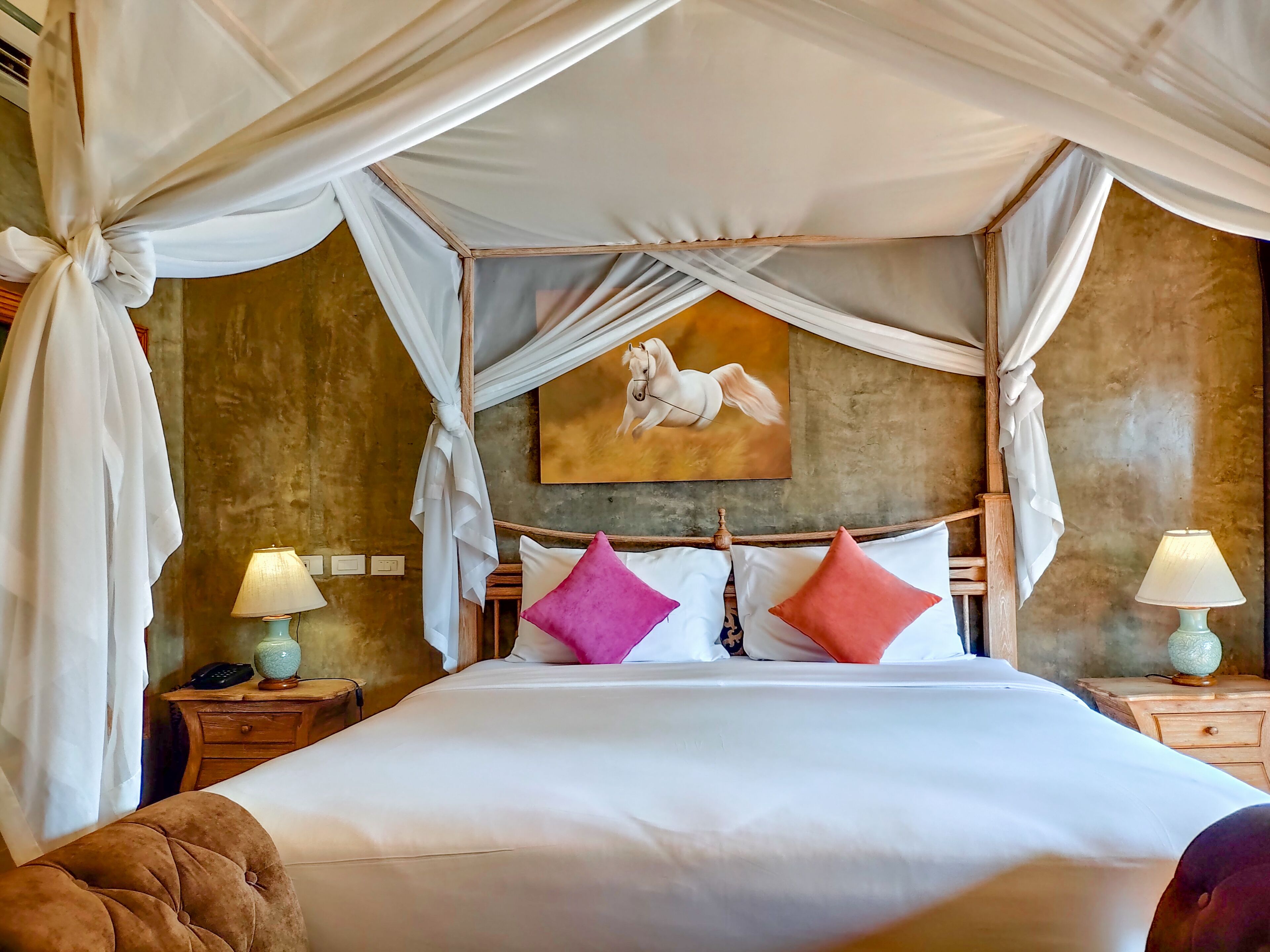 A bed with a canopy, a painting on the wall, two bedside tables with lamps, and a wooden headboard.