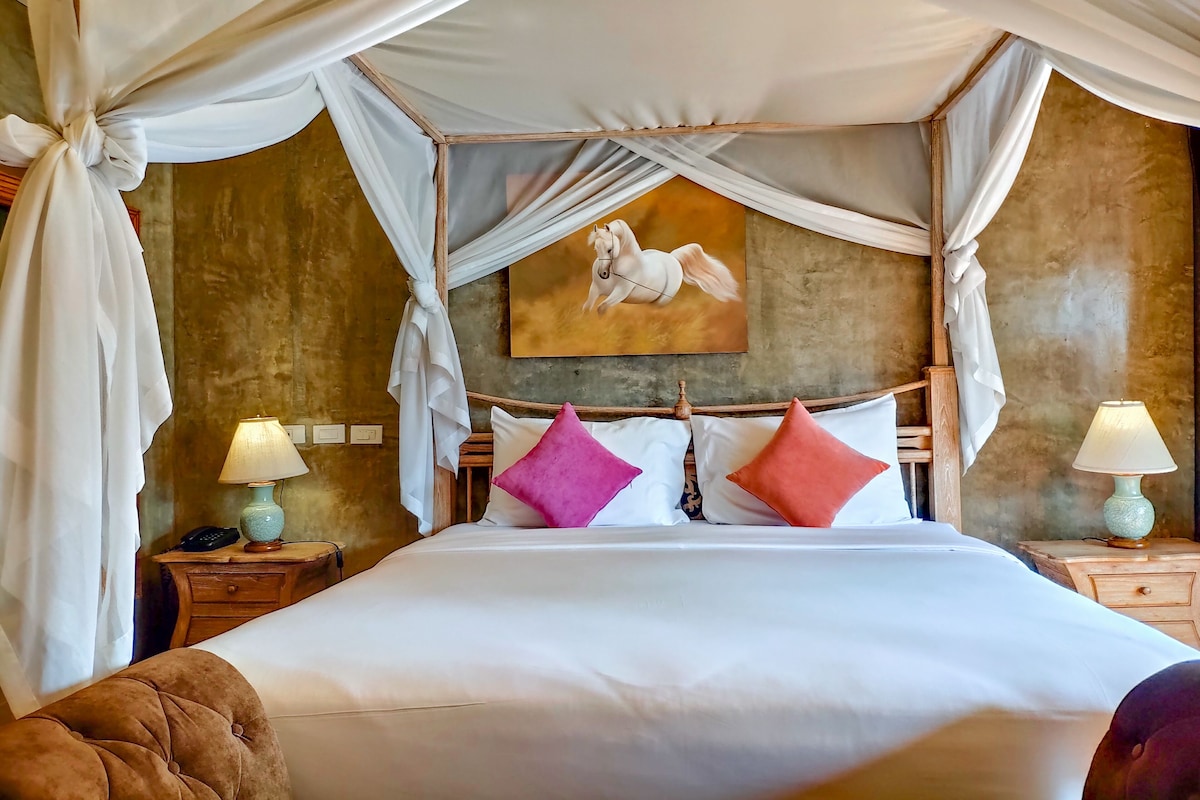 Een bed met hemelbed, een schilderij aan de muur, twee nachtkastjes met lampen en een houten hoofdeinde.