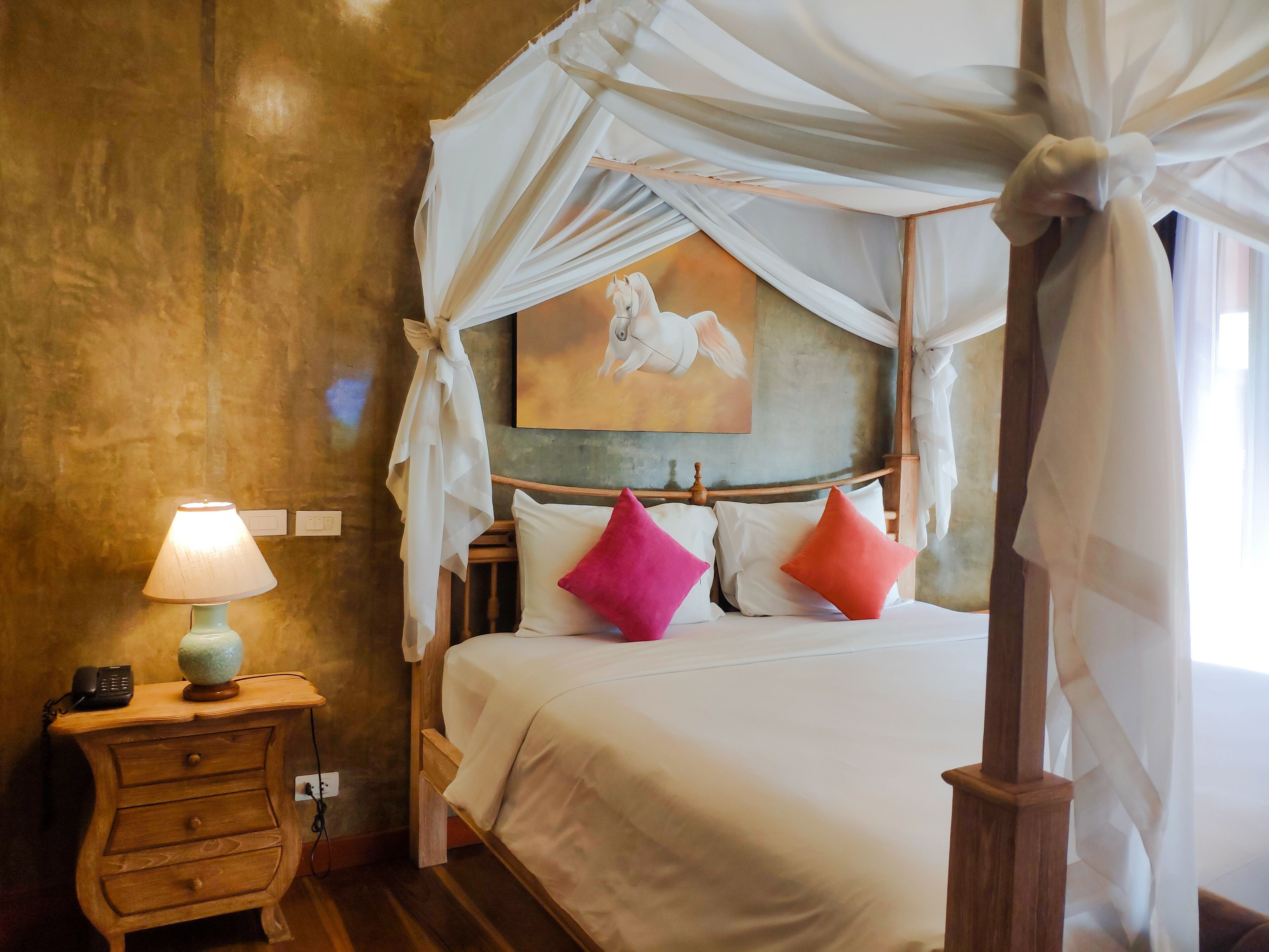 A bedroom with a canopy bed, a bedside table with a lamp, and a painting on the wall.