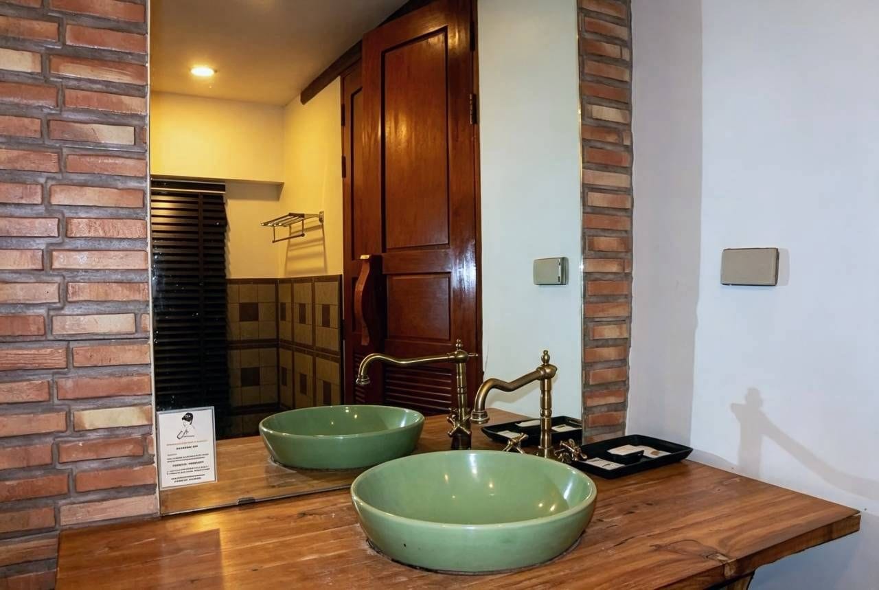 A bathroom with a wooden vanity, two green ceramic sinks, and a mirror reflecting the room.