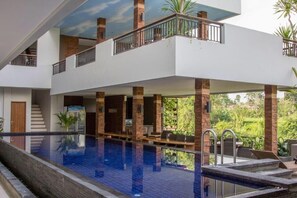 A modern building with a large indoor swimming pool, multiple balconies, and a view of greenery. - Puri Padma Hotel (Ubud)