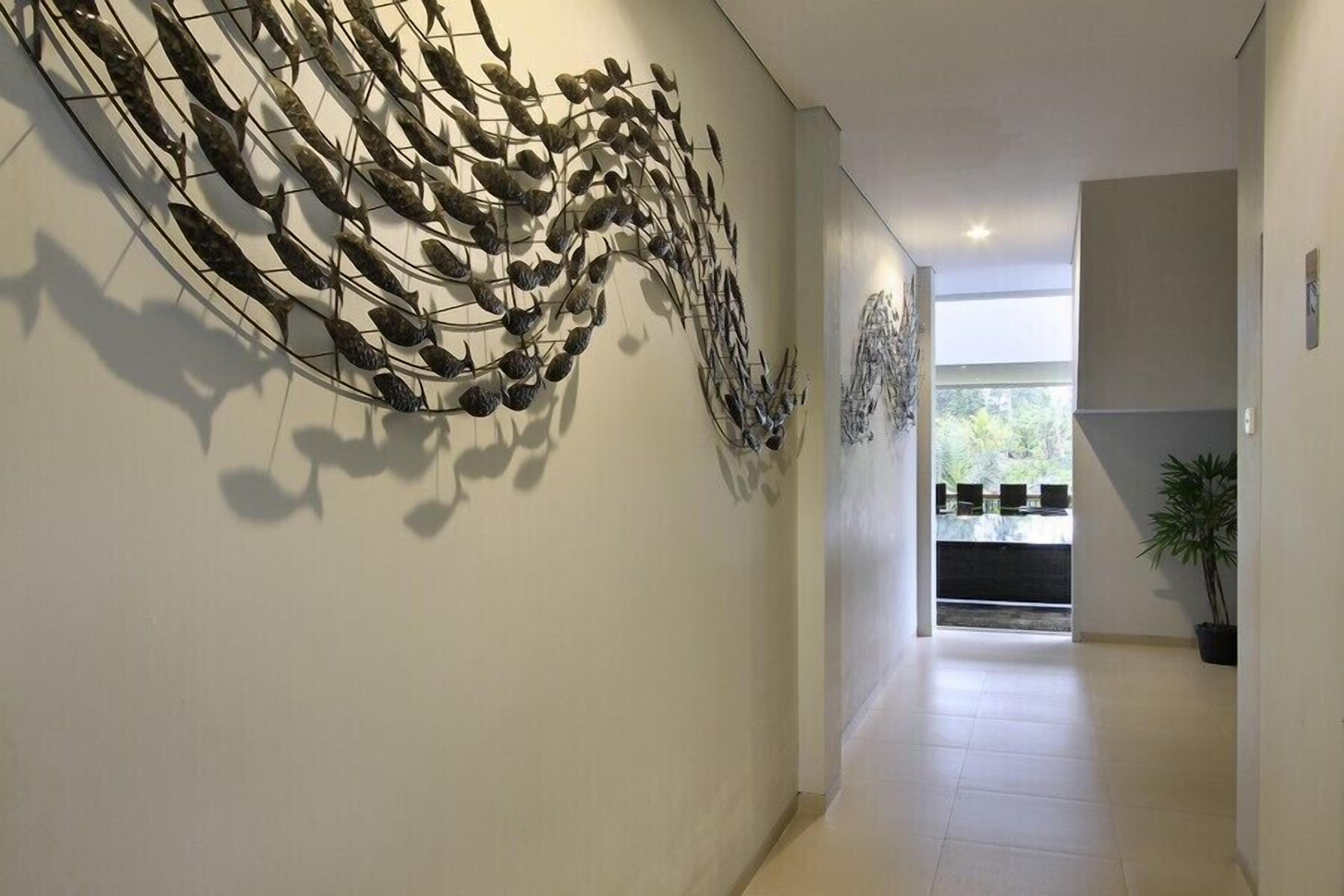 A hallway with a modern art installation on the wall, a potted plant, and a view into another room.