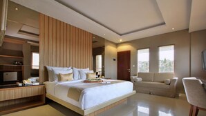 A modern hotel room with a large bed, a sofa, a TV, and a desk.