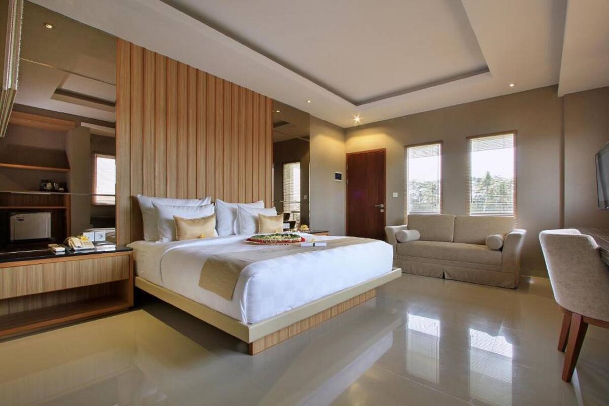 A modern hotel room with a large bed, a sofa, a TV, and a desk.