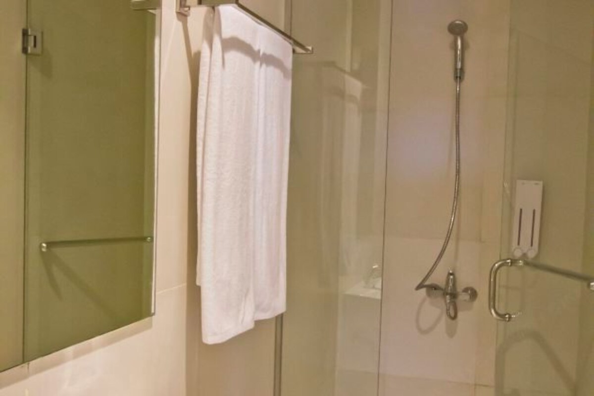 A glass-enclosed shower with a handheld showerhead and a towel rack with a white towel.
