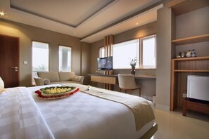 A hotel room with a large bed, a desk with a computer, a television, and a small seating area. - Puri Padma Hotel (Ubud)