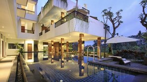 Un immeuble moderne à plusieurs étages, doté d’une piscine sur le toit, d’un espace extérieur aménagé et d’un jardin luxuriant.