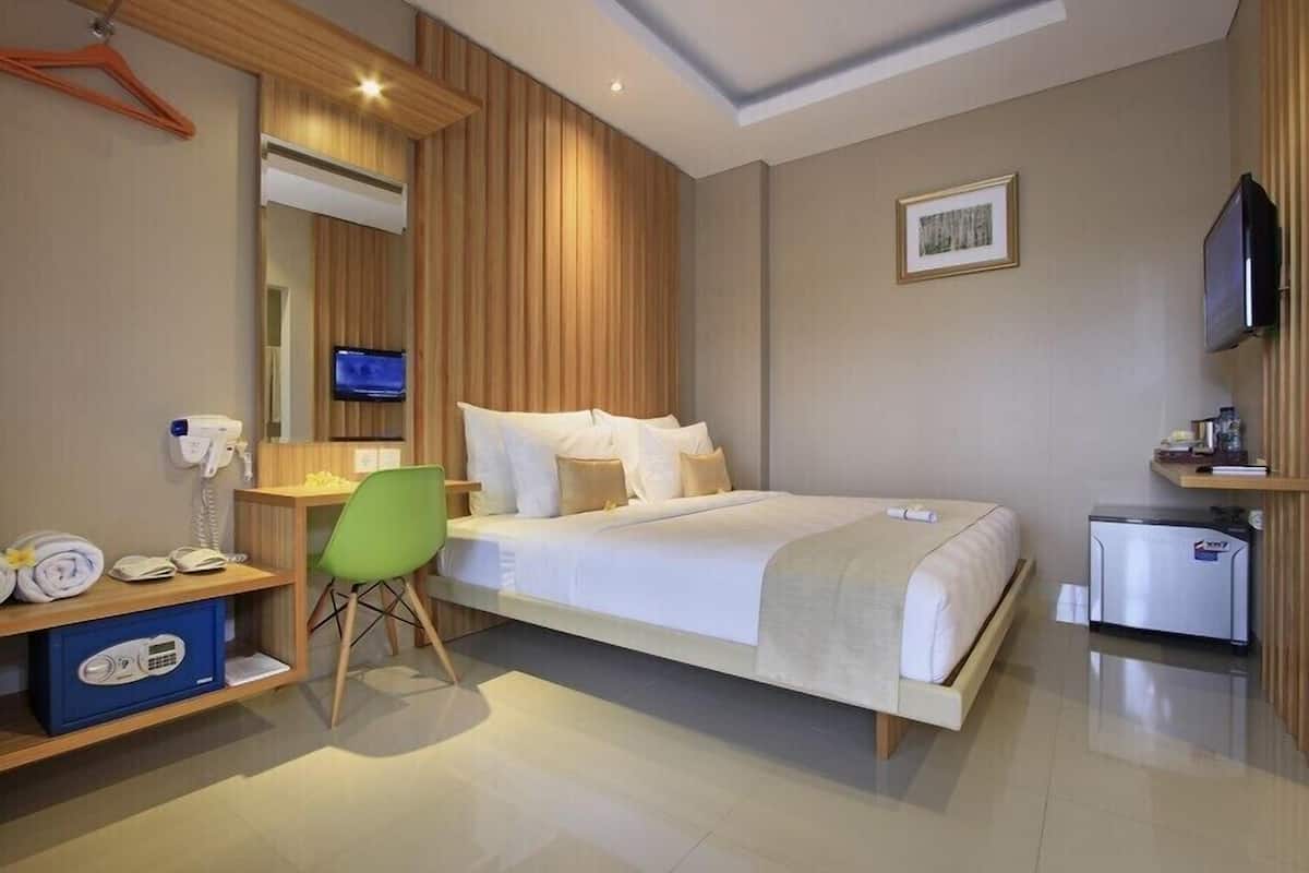 A hotel room with a bed, a desk, a chair, a TV, a mini-fridge, and a wardrobe.