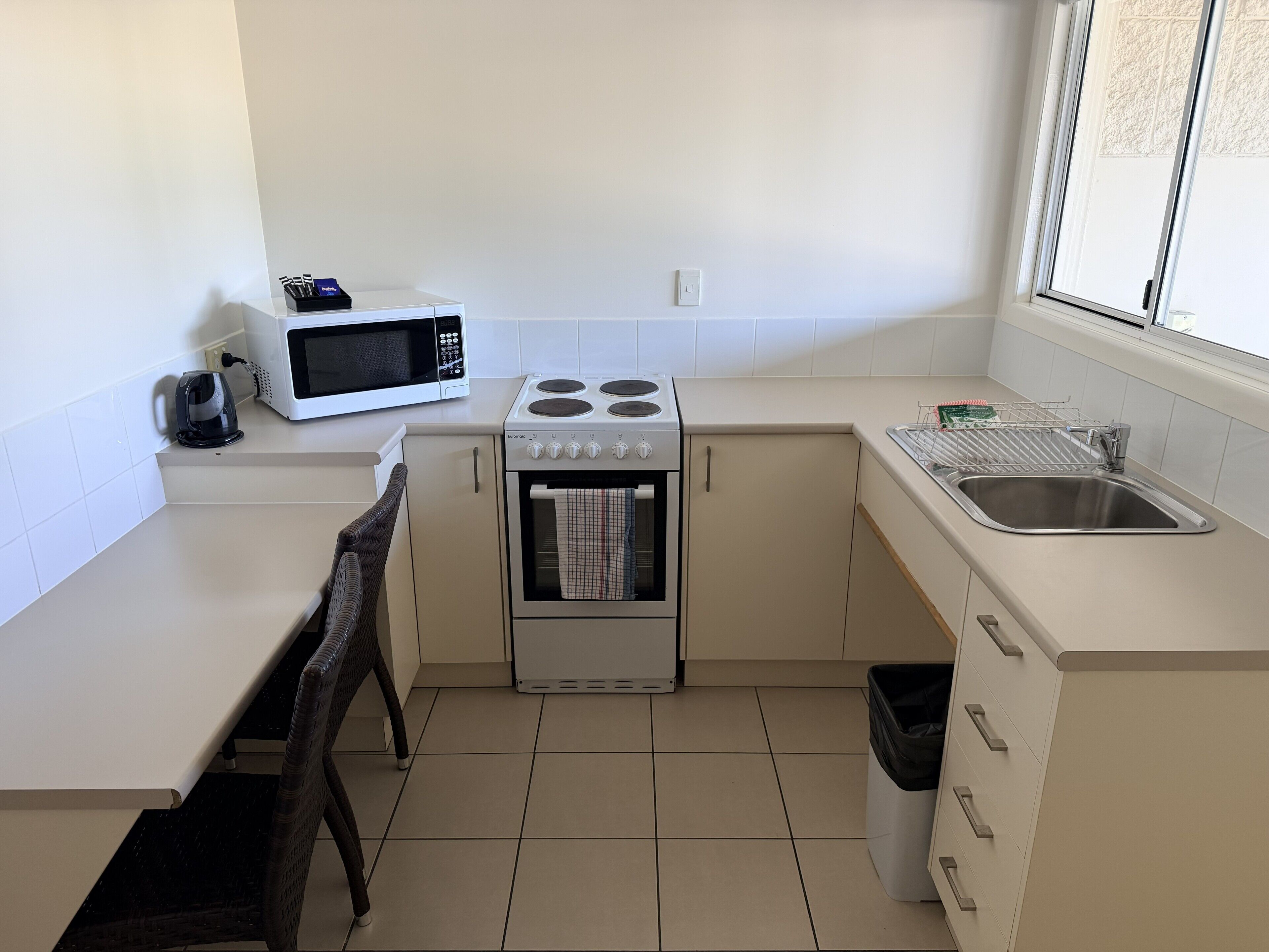 A compact kitchen with a stove, microwave, sink, and a window.