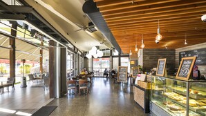 A spacious cafe with a modern interior, featuring a counter with baked goods, seating areas, and a view of the outdoors. - Nightcap at Golden Beach Tavern (Caloundra)