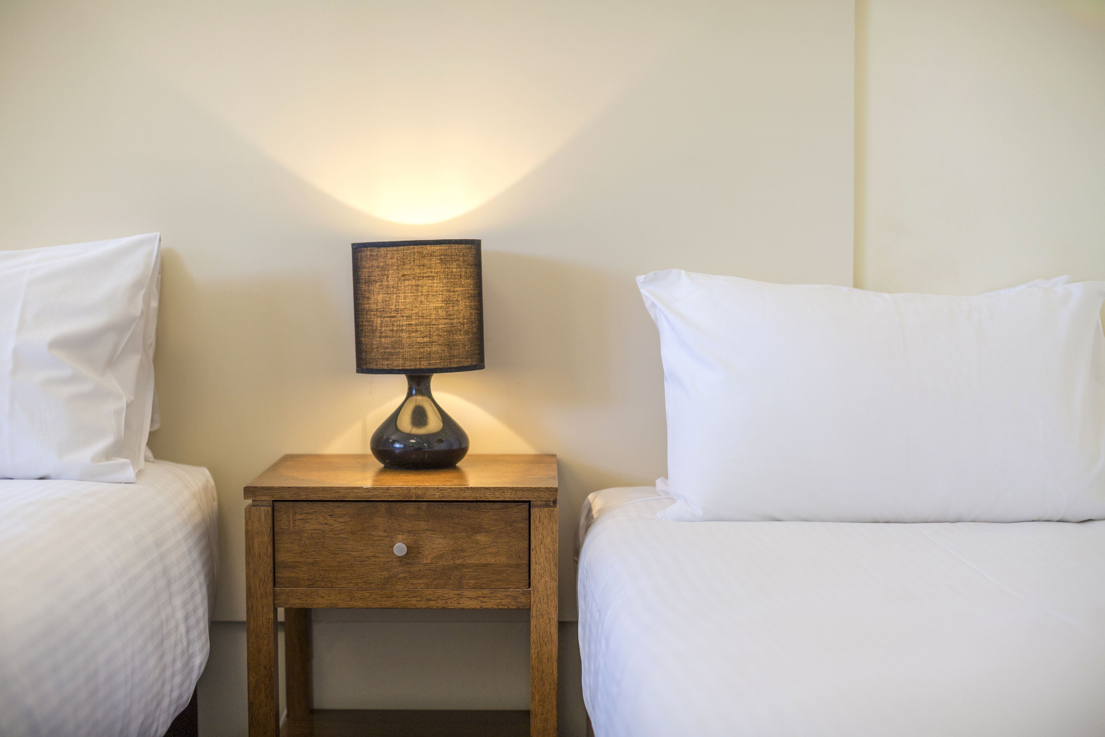 Une chambre d’hôtel avec deux lits simples, une table de chevet avec une lampe et un tiroir en bois.
