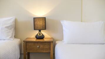 Une chambre d’hôtel avec deux lits simples, une table de chevet avec une lampe et un tiroir en bois.