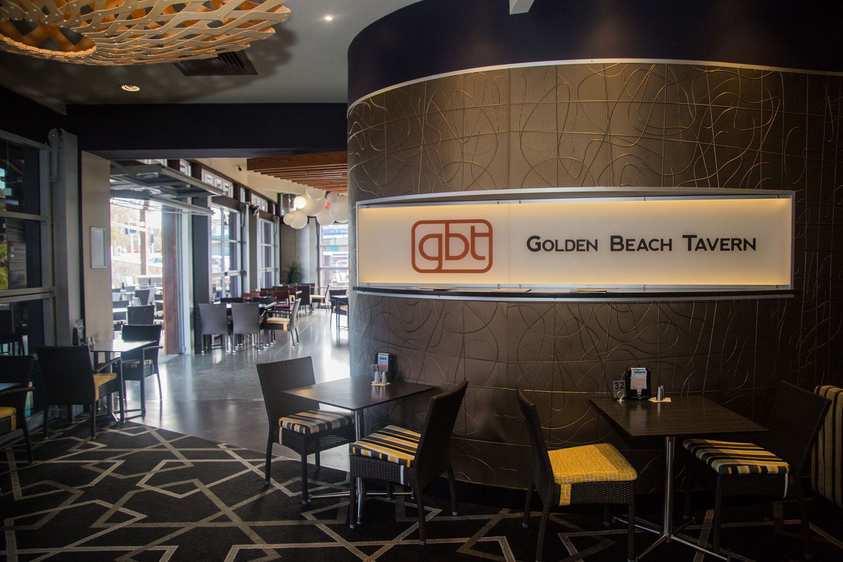 A modern interior of the Golden Beach Tavern with a curved reception desk, seating area, and a patterned floor.