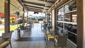 An outdoor patio with tables and chairs, a ceiling fan, and a view of the street. - Nightcap at Golden Beach Tavern (Caloundra)