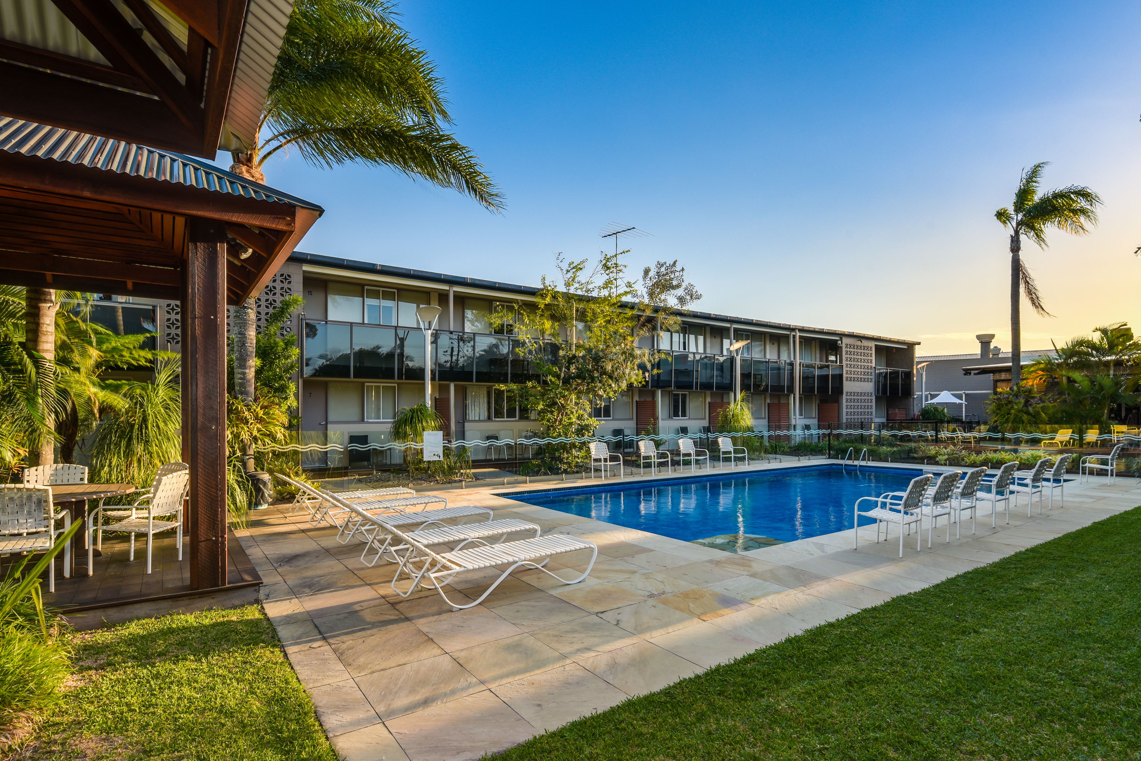 A hotel with a swimming pool, outdoor seating, and a covered patio area.