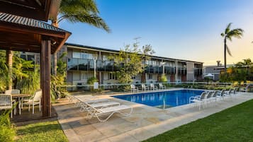 A hotel with a swimming pool, outdoor seating, and a covered patio area.