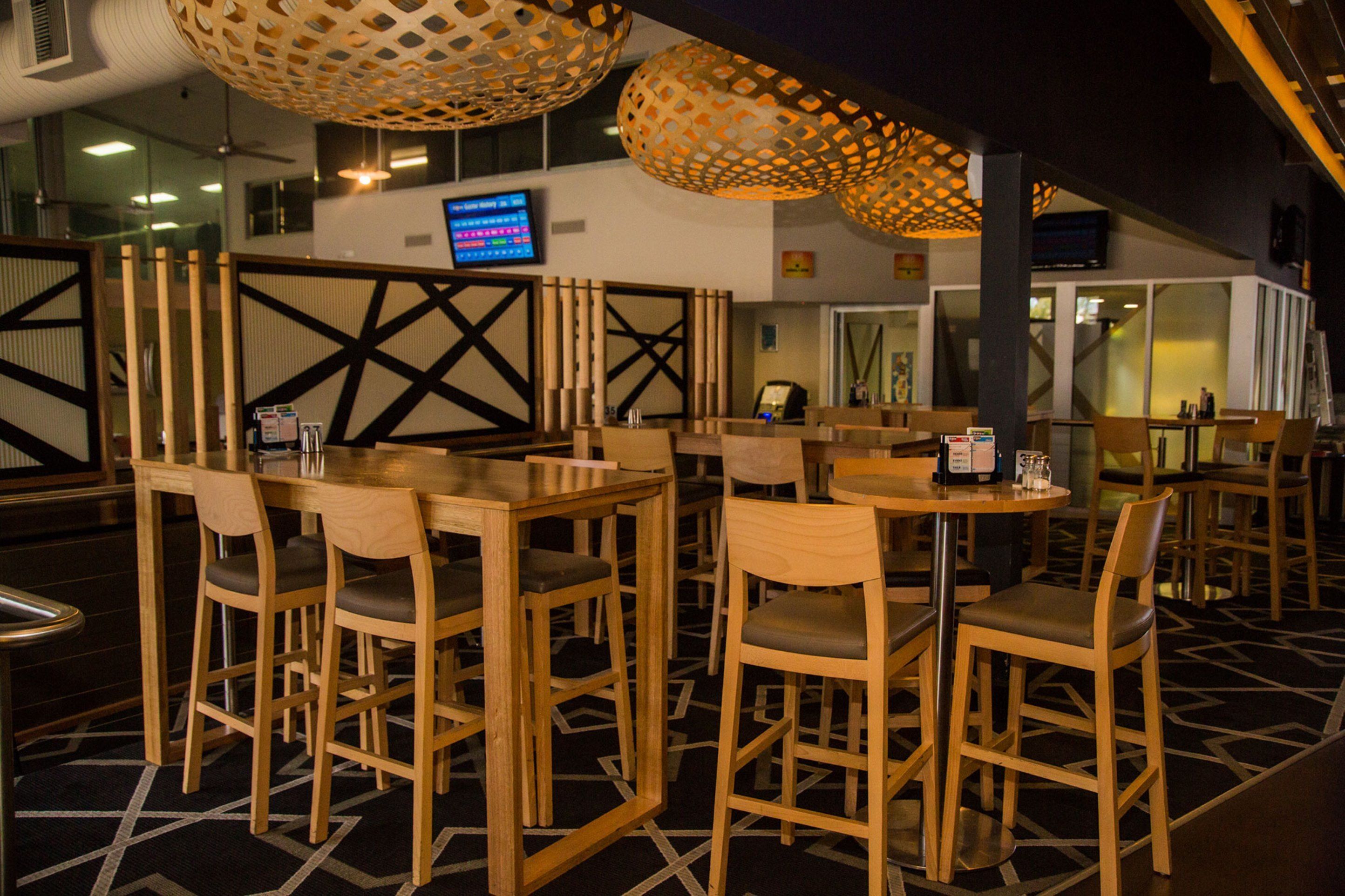 A restaurant with wooden tables and chairs, a digital menu board, and decorative hanging lamps.