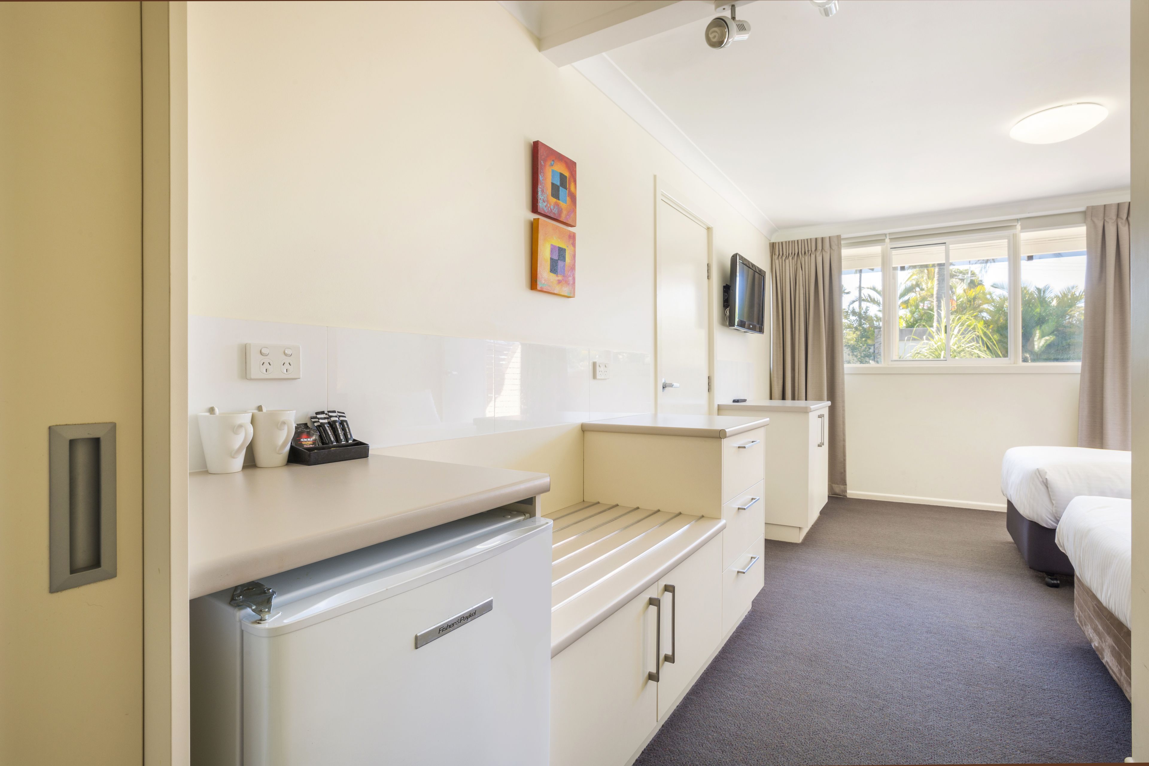 A hotel room with a kitchenette, a bed, a TV, and a window with curtains.
