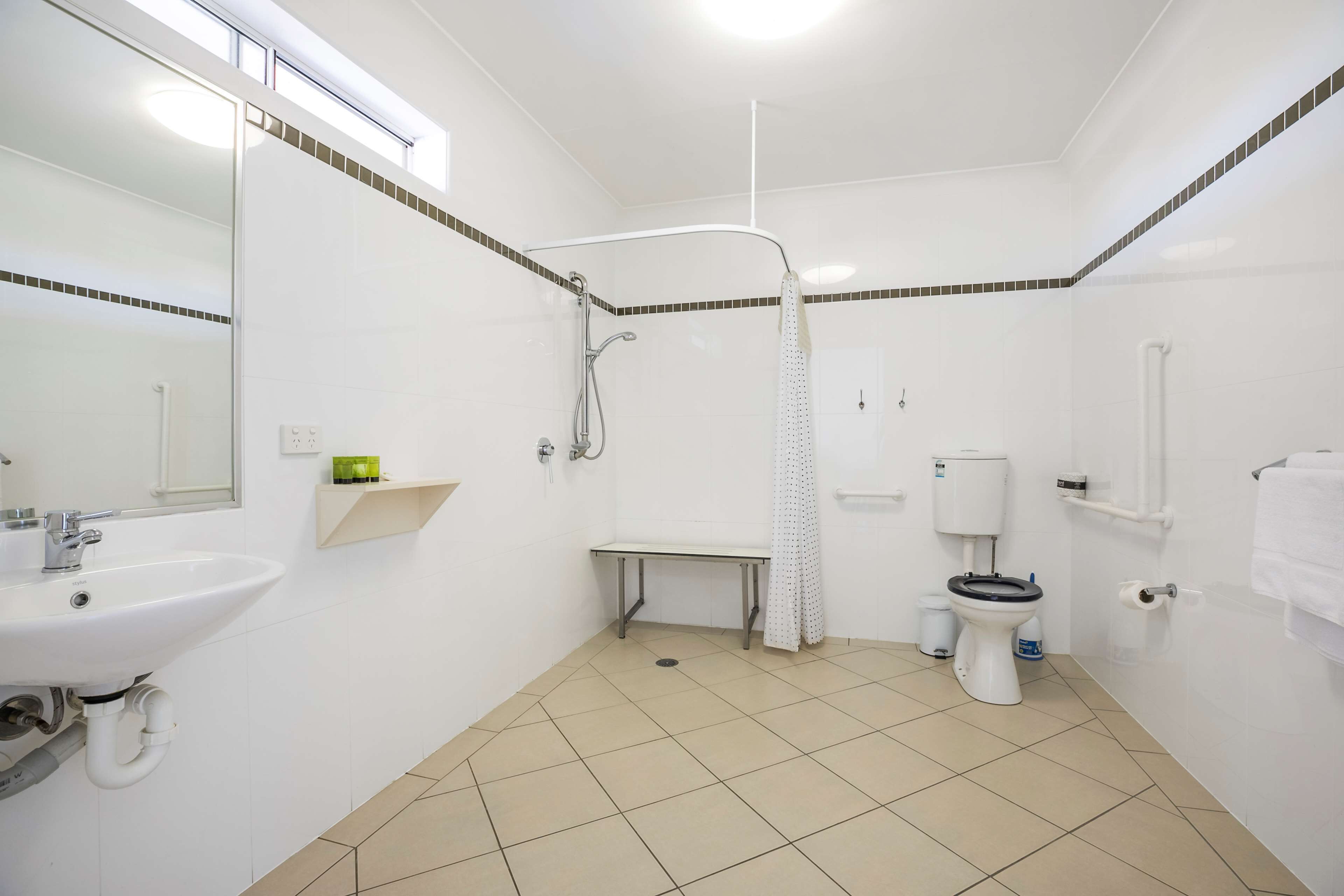 A bathroom with a sink, toilet, shower, and a bench.