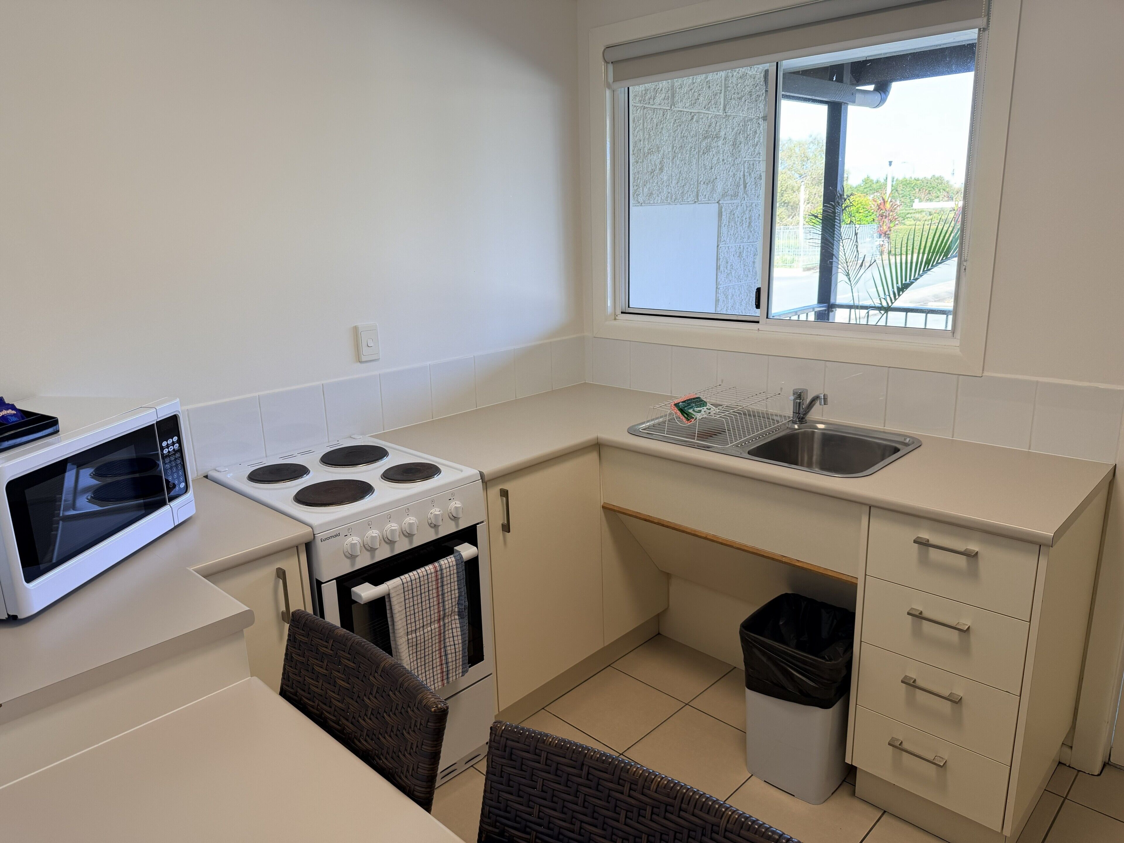 A compact kitchen with a microwave, stove, sink, and window.