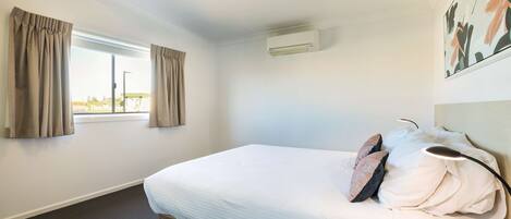 A hotel room with a bed, curtains, an air conditioning unit, and a window.