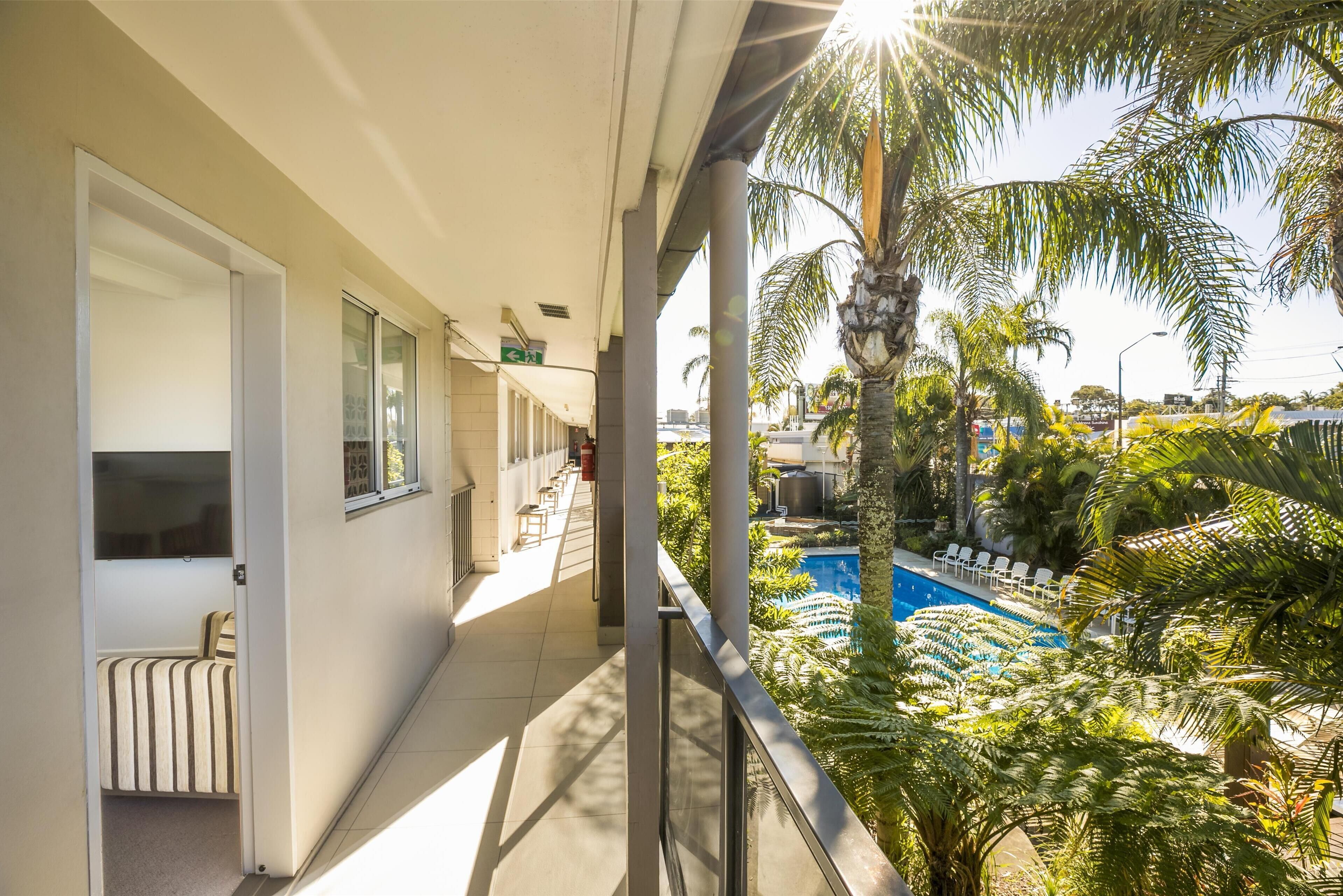 A balcony with a view of a swimming pool, palm trees, and a building with a glass door and striped curtains.