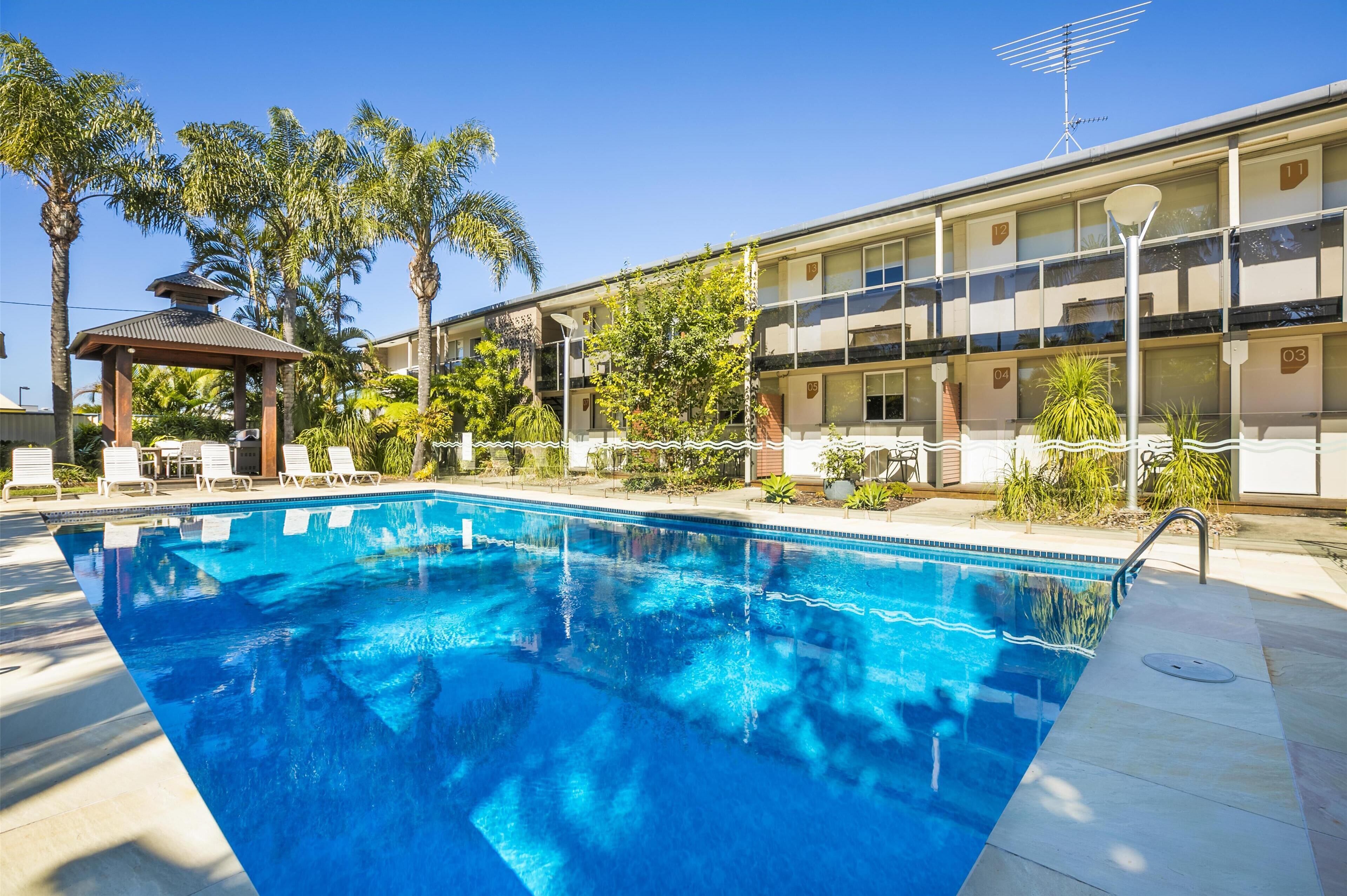 A swimming pool with lounge chairs, a gazebo, and a building with numbered balconies.