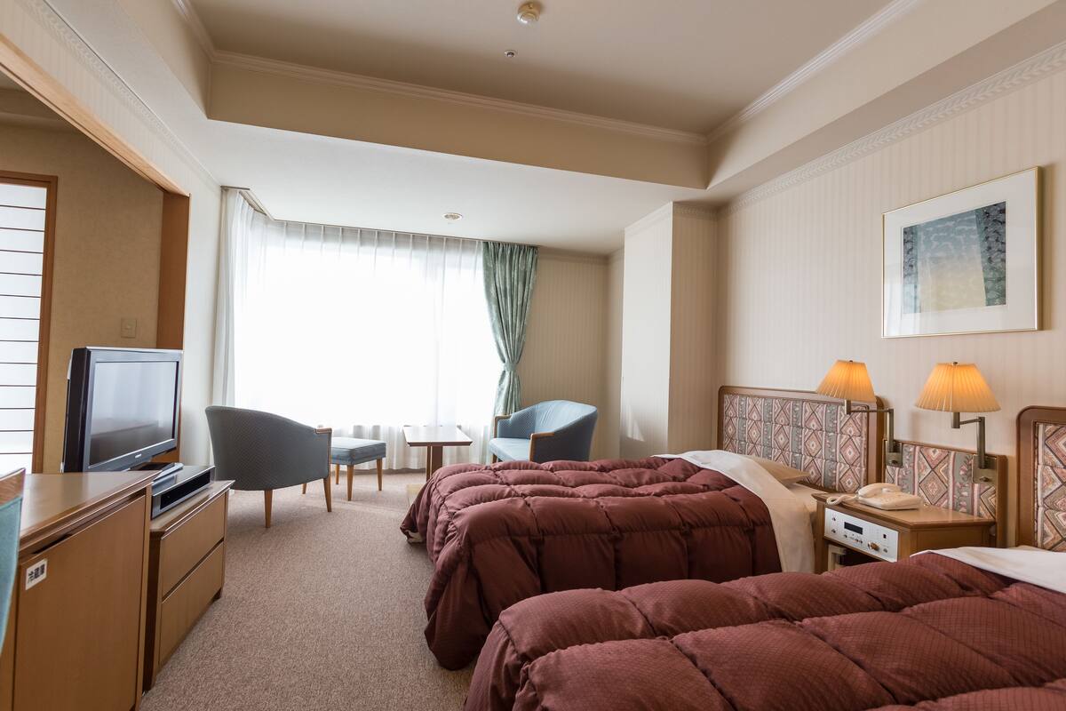 Een hotelkamer met twee bedden, een bureau met televisie, een stoel, een klein tafeltje en een lamp.