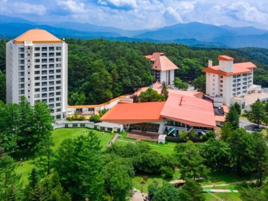 A hotel complex with multiple buildings, surrounded by lush greenery and mountains in the background.