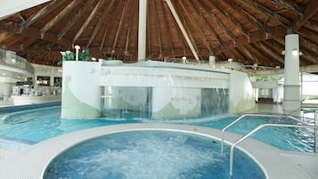An indoor swimming pool with a waterfall feature, surrounded by a covered area with a wooden ceiling.