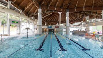 An indoor swimming pool with clear lanes, a wooden ceiling, and a reception area with chairs and tables.