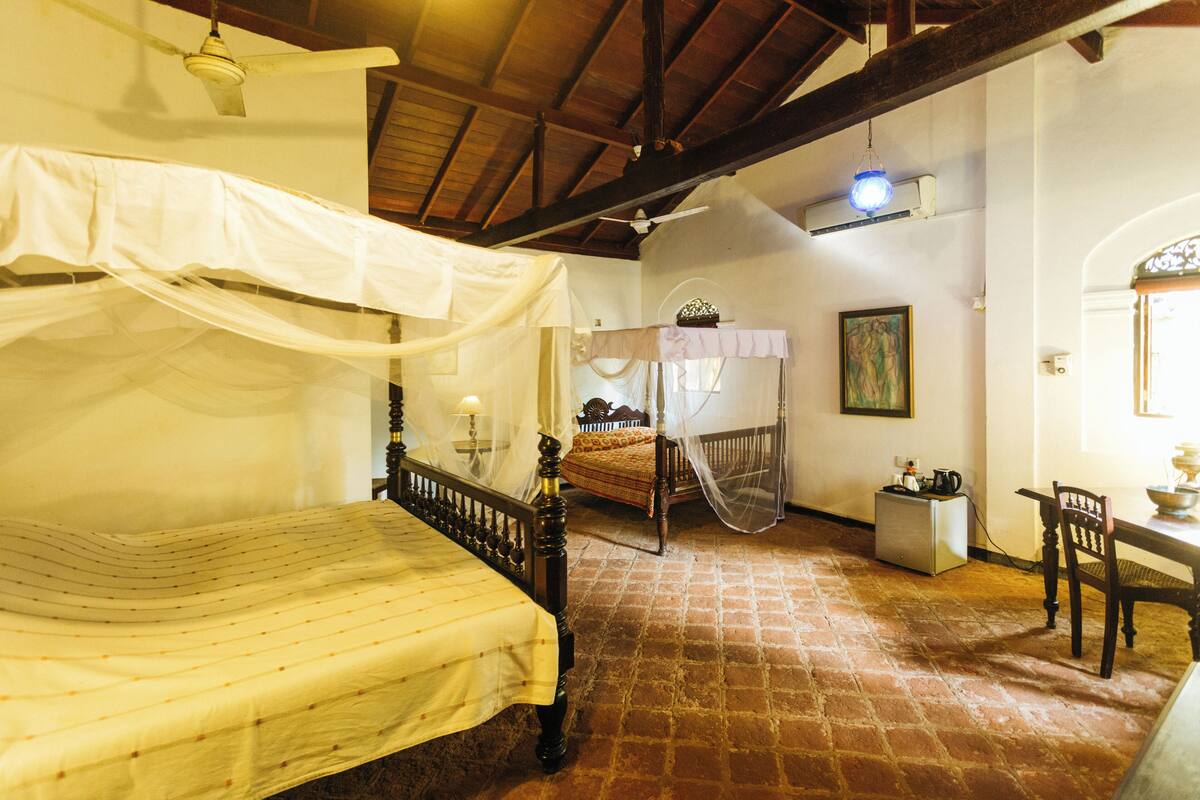 A traditional room with a four-poster bed, a wooden chair, a small table, and a brick floor.