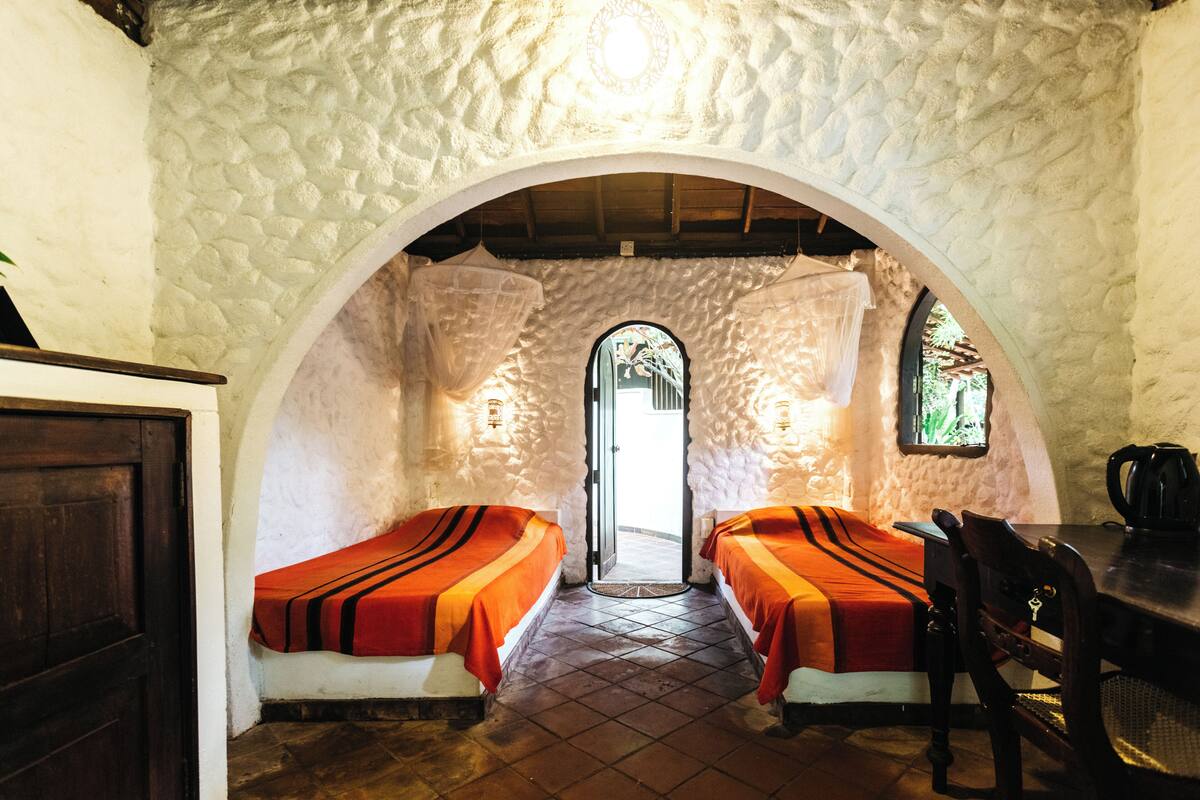 A room with two beds, a wooden table, and a stone wall.