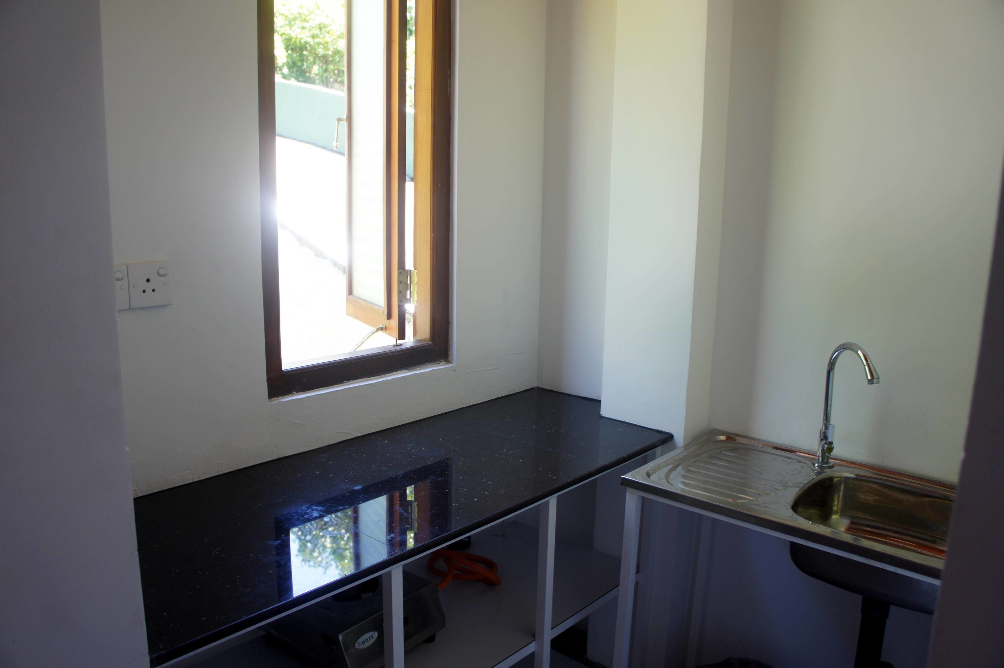 A small kitchen with a black countertop, a window, and a sink.