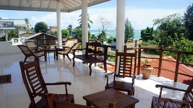A covered outdoor seating area with wooden furniture and a view of the ocean. - Sam's Guest House (Unawatuna)