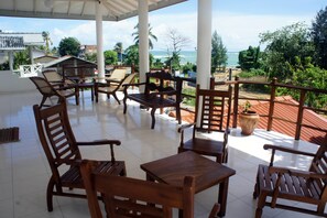 A covered outdoor seating area with wooden furniture and a view of the ocean. - Sam's Guest House (Unawatuna)