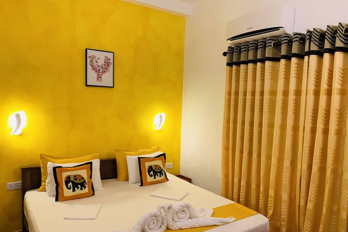 Une chambre d’hôtel avec un lit, deux oreillers ornés de motifs d’éléphants, un tableau encadré au mur et un rideau à rayures.