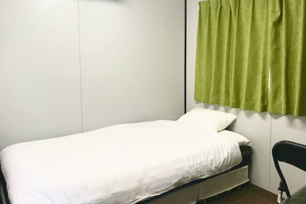 A single bed with white bedding, a green curtain, and a white air conditioning unit on the wall.