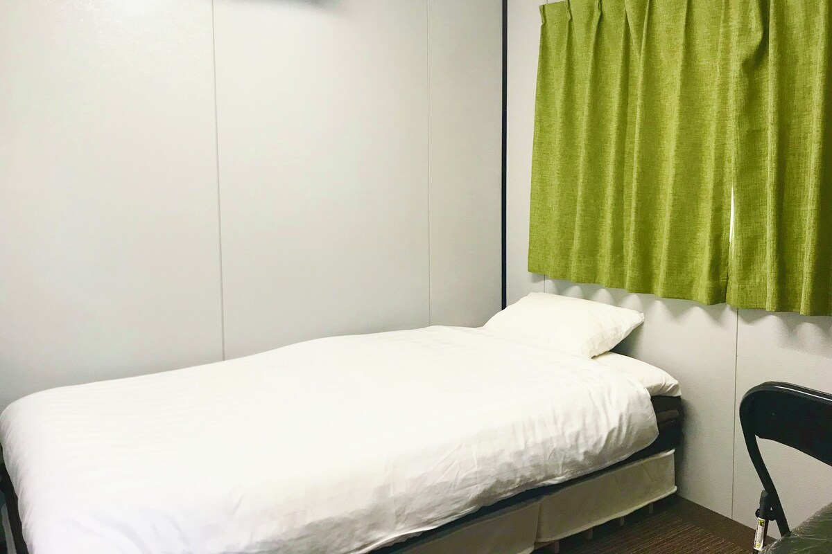 A single bed with white bedding, a green curtain, and a wall-mounted air conditioner.