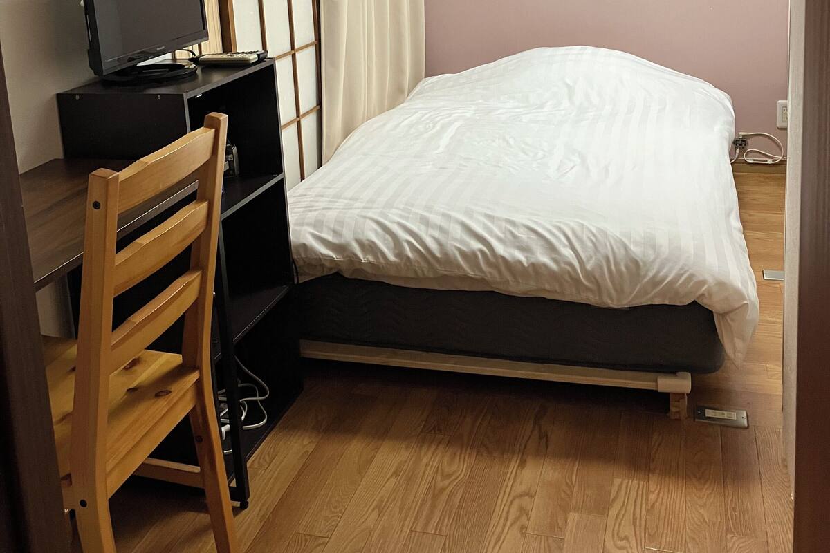 A bedroom with a bed, a desk with a computer, a chair, and a window with curtains.