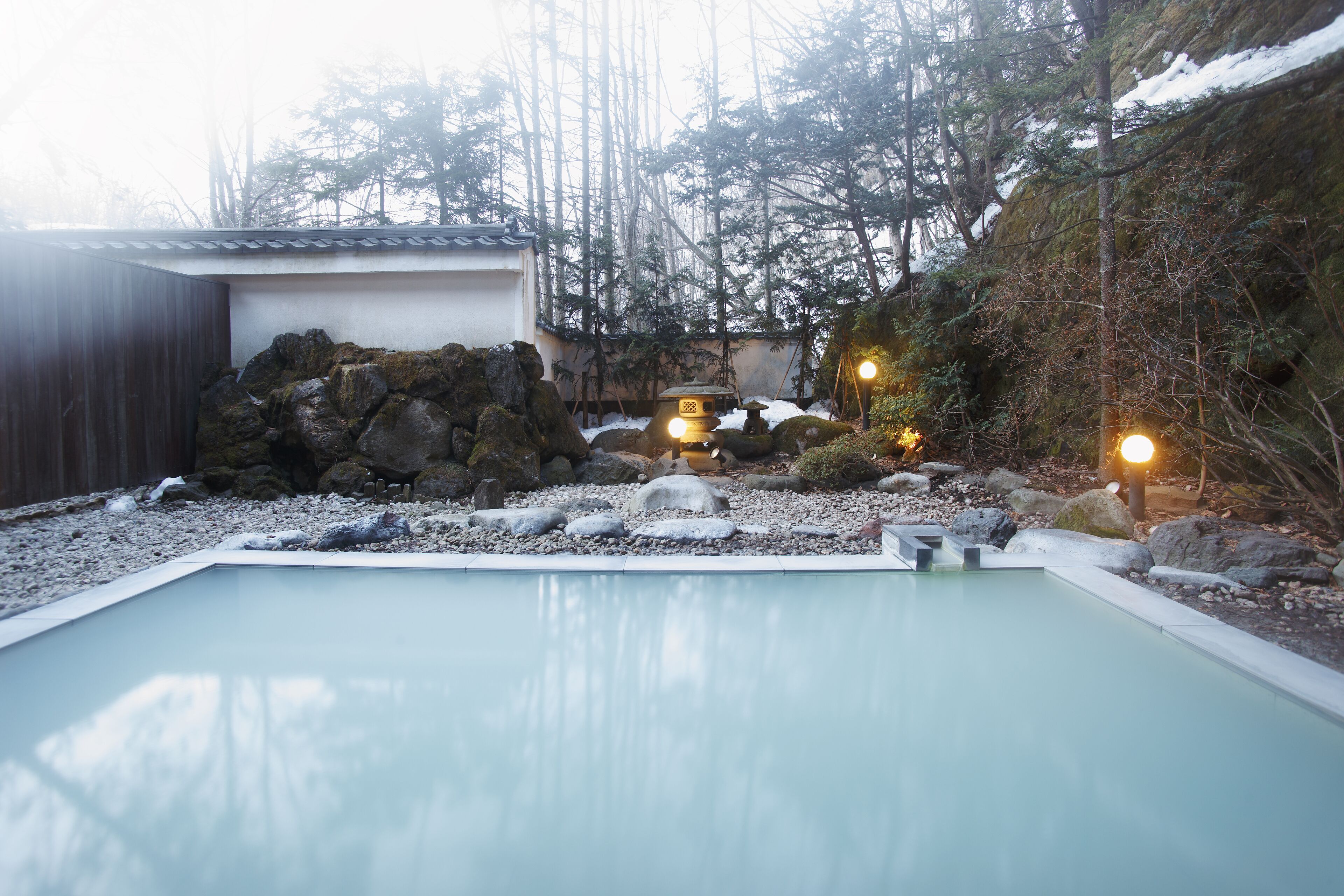 A serene outdoor pool area with a clear view of the surrounding landscape, including a traditional building and a rocky terrain.